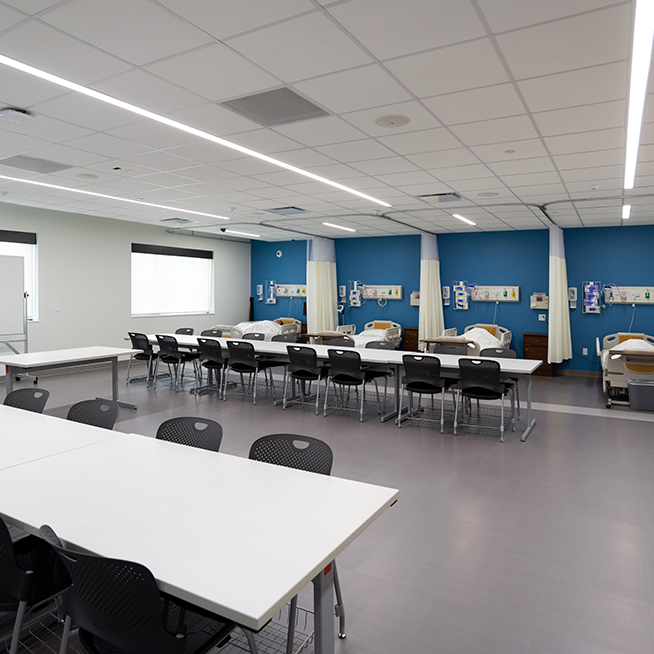 Galen Austin simulation lab. Medical mannequins are on hospital beds in background, with long tables in chairs in front.