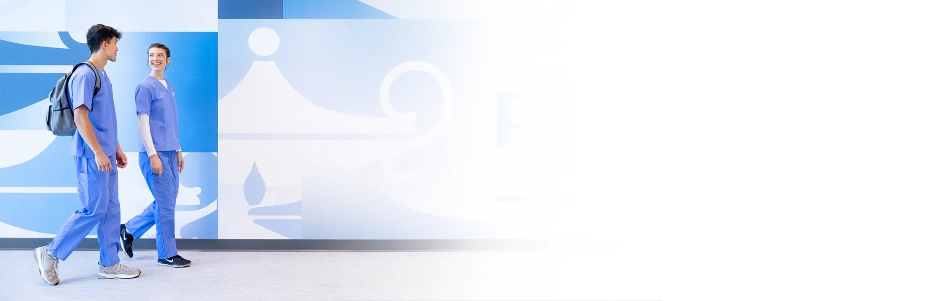 two students, a male and female, walking along a wall at a Galen campus and talking to each other.