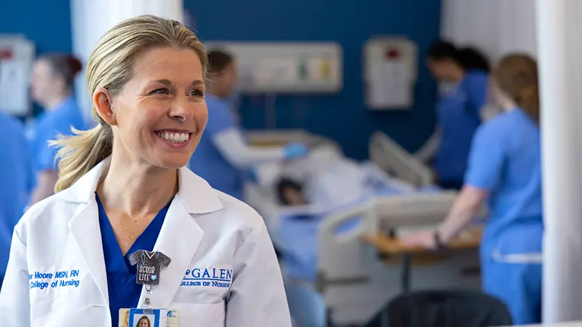 woman nursing instructor smiling at camera with simulation lab activities happening in background