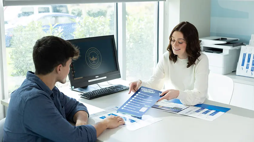 A female admissions counselor meeting with a young man in a sunlit office at Galen, showing him a checklist.