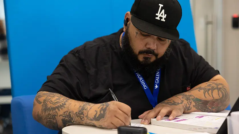 A male Galen student does homework, wearing a LA Dodgers cap