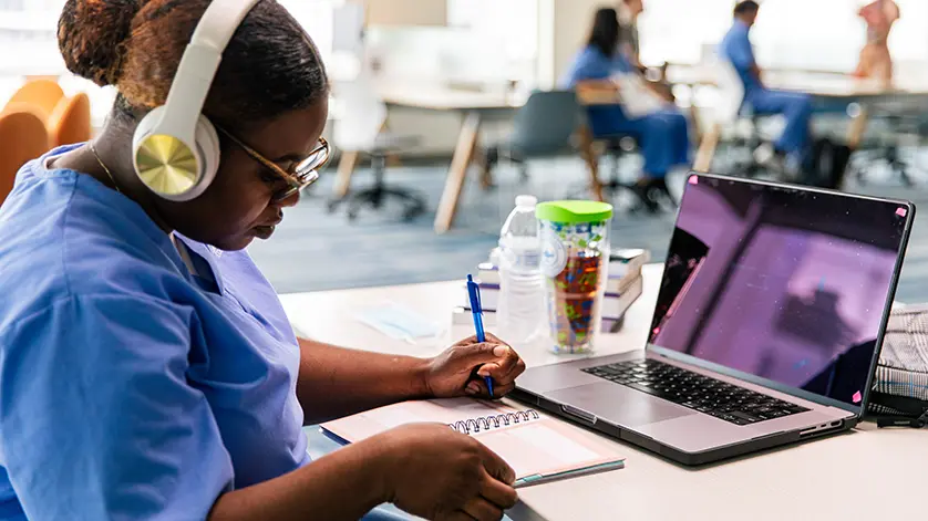 a young female Galen student studies with her laptop while wearing headphones