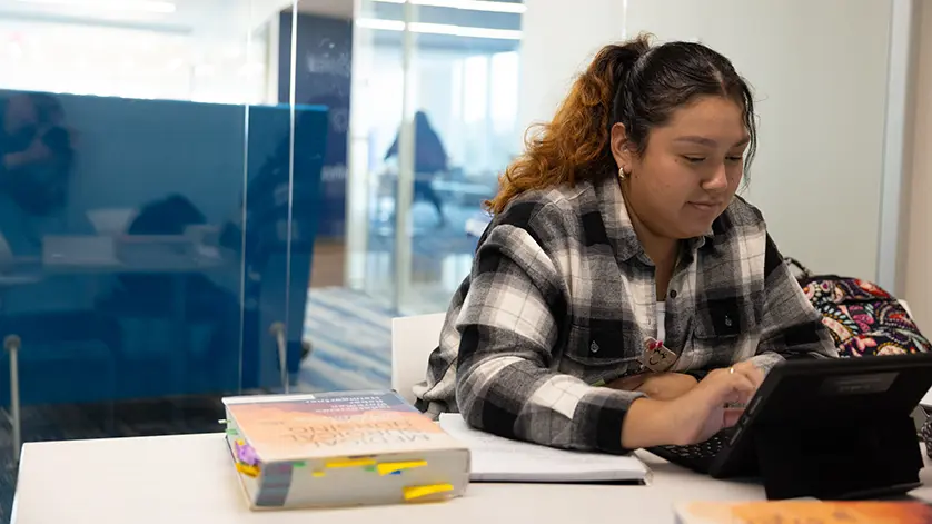 a Galen student studies with her tablet, with a textbook on the table next to her.