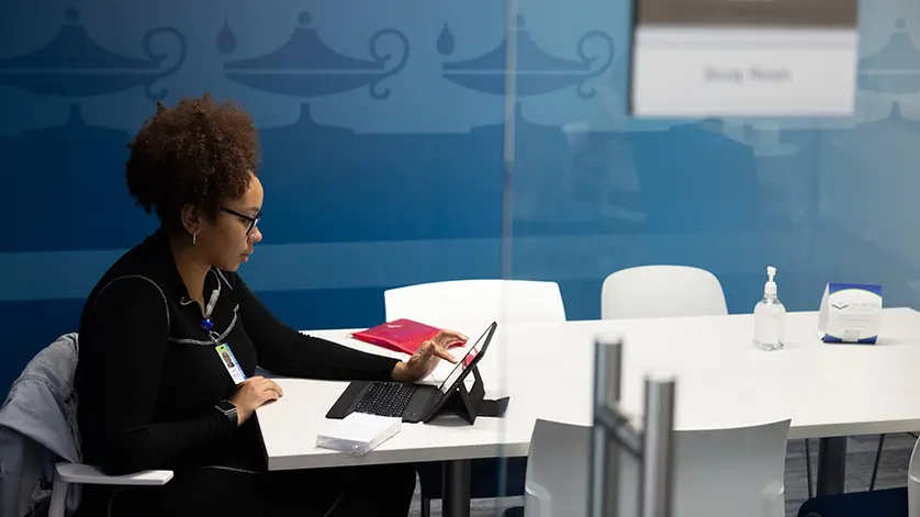 a young female Galen student studies with her laptop in front of a dark blue wall