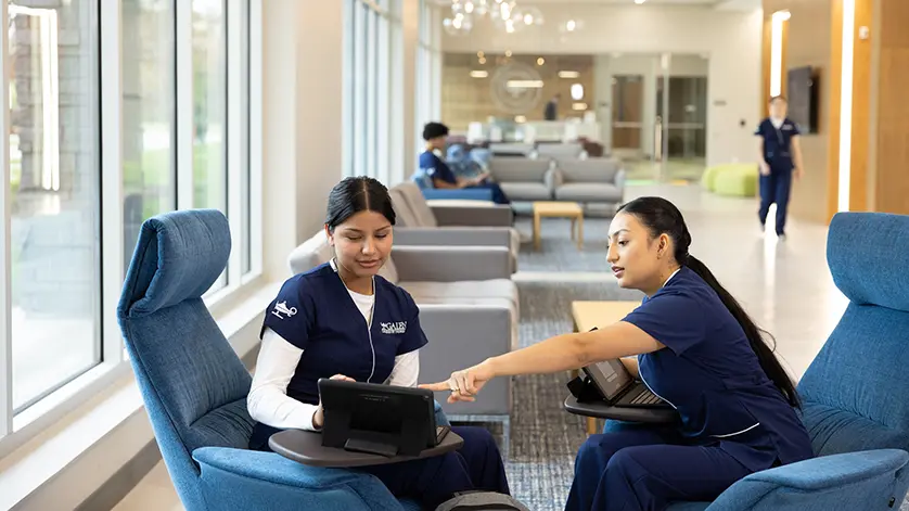Two female students in dark blue scrubs study in a commons area of a Galen campus.